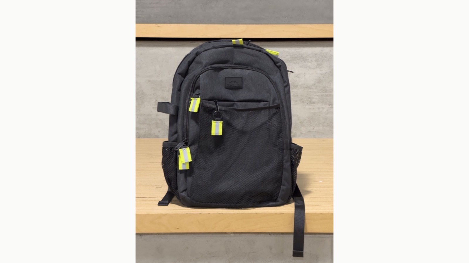 The finished black backpack photographed head on, with bright yellow and grey reflective zipper pulls on every zipper and a mesh front pocket.