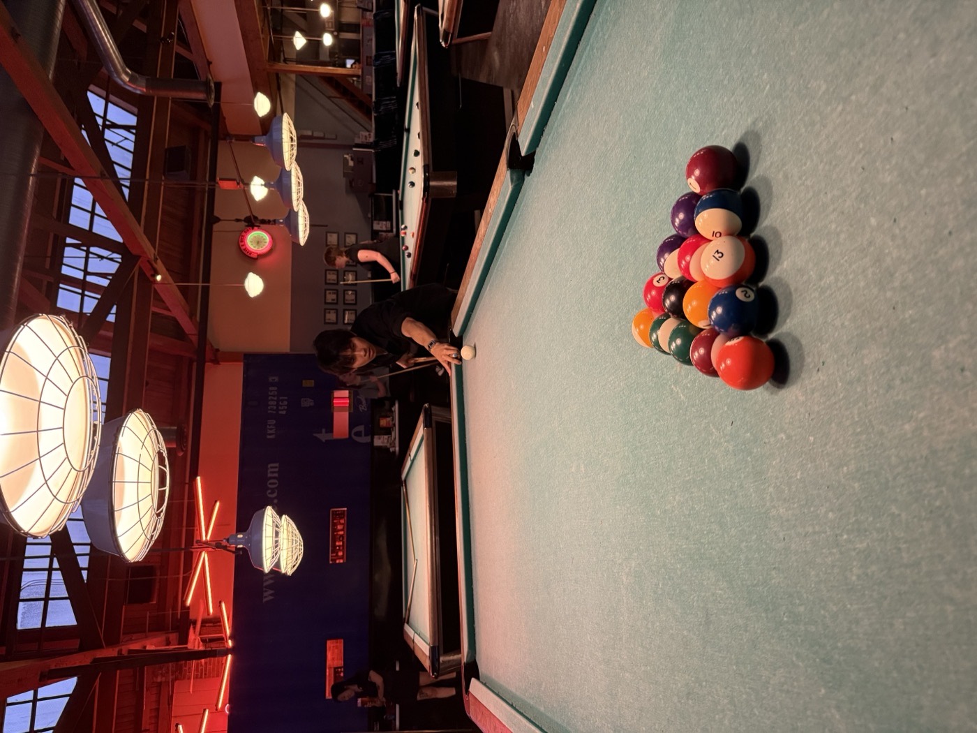 Justis lining up a shot at a rack of pool tables under warm hanging lamps.