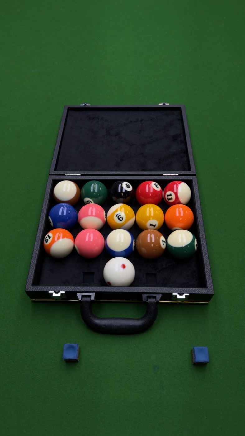 A travel case of billiard balls and chalk, open on the felt.
