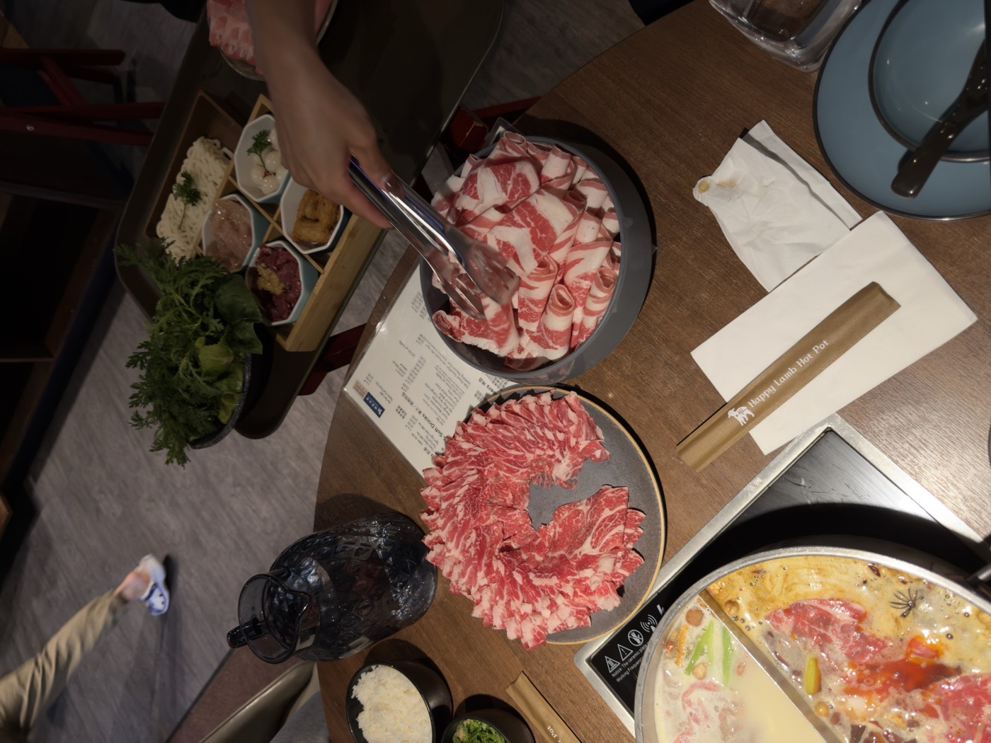 Thinly sliced beef fanned on a plate beside a hot pot at a shabu shabu dinner.