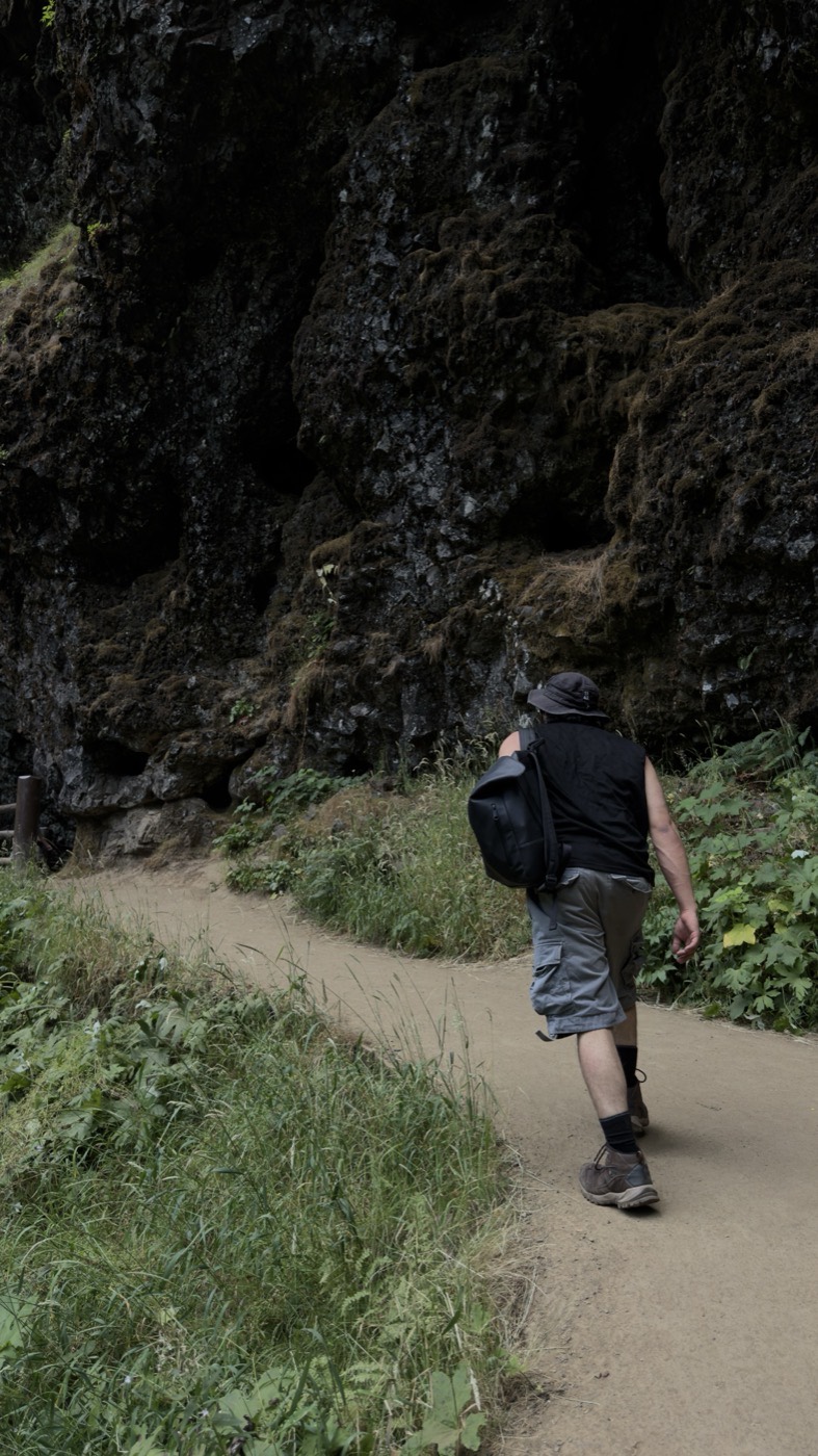 Justis hiking a narrow trail beneath a moss covered rock wall.